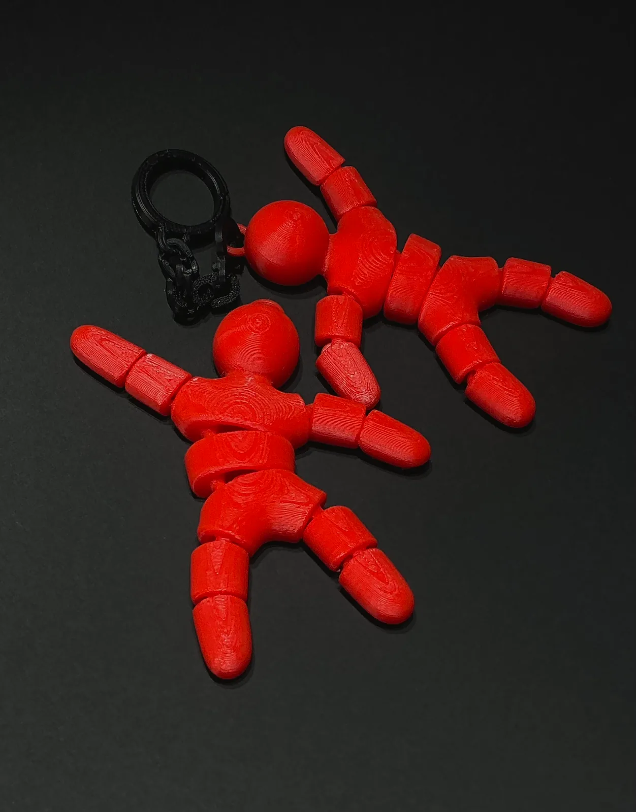 Dos llaveros temáticos articulados en rojo con las piezas del cuerpo unidas por rótulas y la argolla negra en la misma pieza, sobre fondo negro — Llaveros e imanes de Solid Lab 3D, Colombia